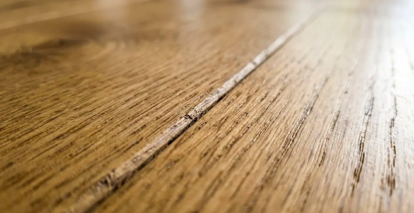 Gros plan extrême sur le grain du bois d'un plancher de chêne, léger espace de deux millimètres visible entre deux planches, lumière latérale naturelle révélant la texture